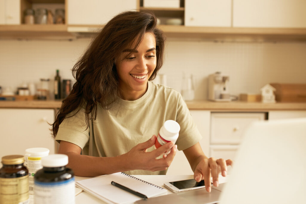 Mulher sorridente segurando frasco de suplemento alimentar, representando uso de magnésio e vitaminas para saúde e energia.