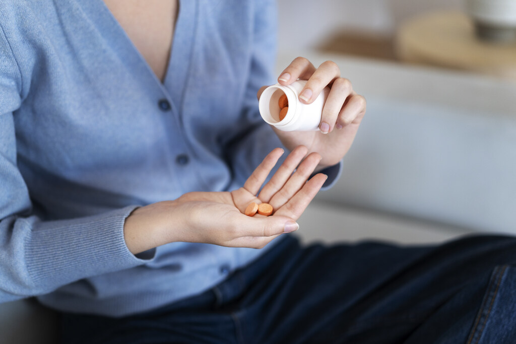 Mãos de uma mulher em primeiro plano segurando um frasco de capsulas e jogando algumas na outra mão